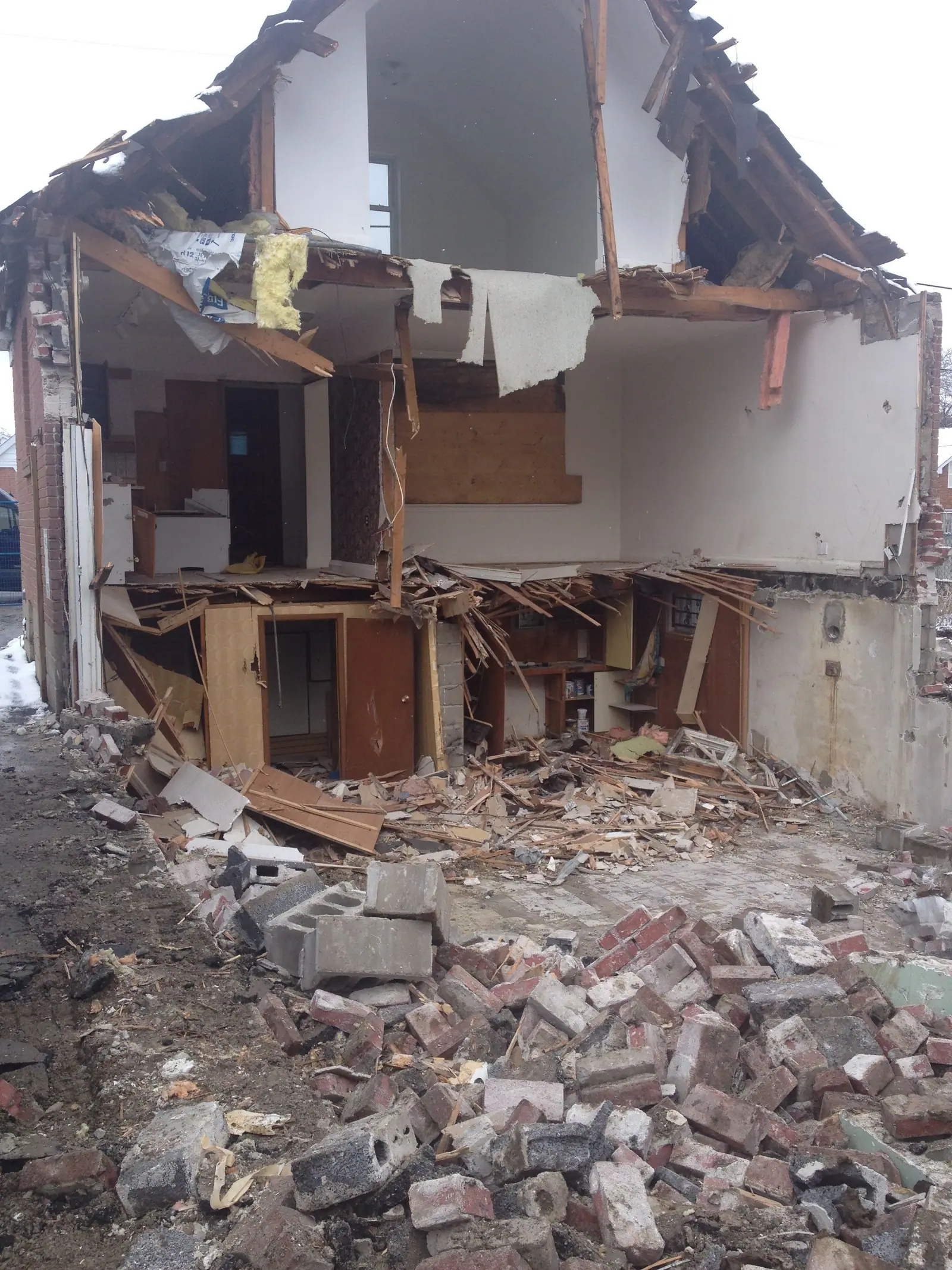 The old house partly pulled down, with brick, plaster and timber piled in front of the open walls.