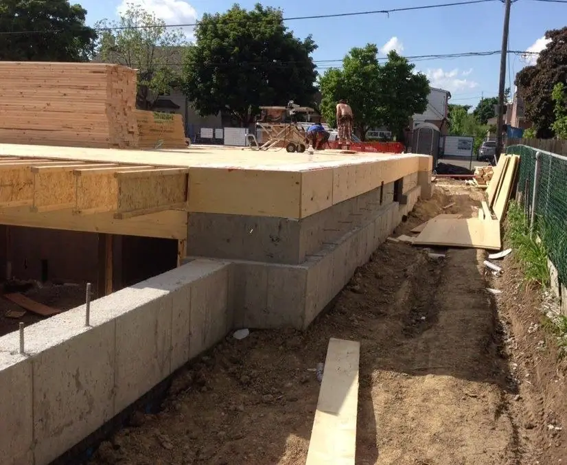 The timber floor frame sitting on the concrete foundation wall, with a stack of lumber on the deck above.