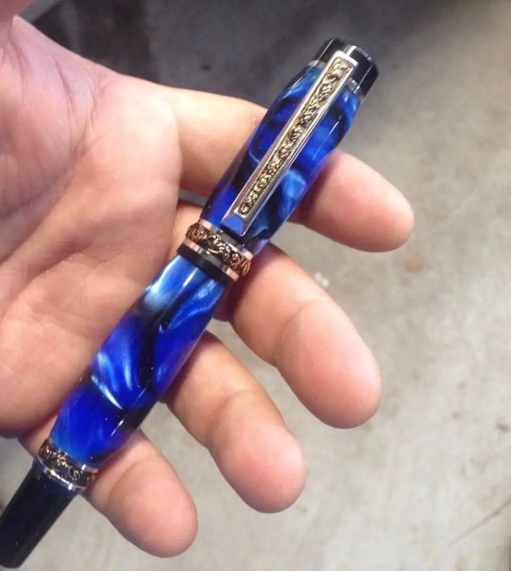 A pen with a marbled blue barrel and ornate gold bands and clip, held in an open palm.