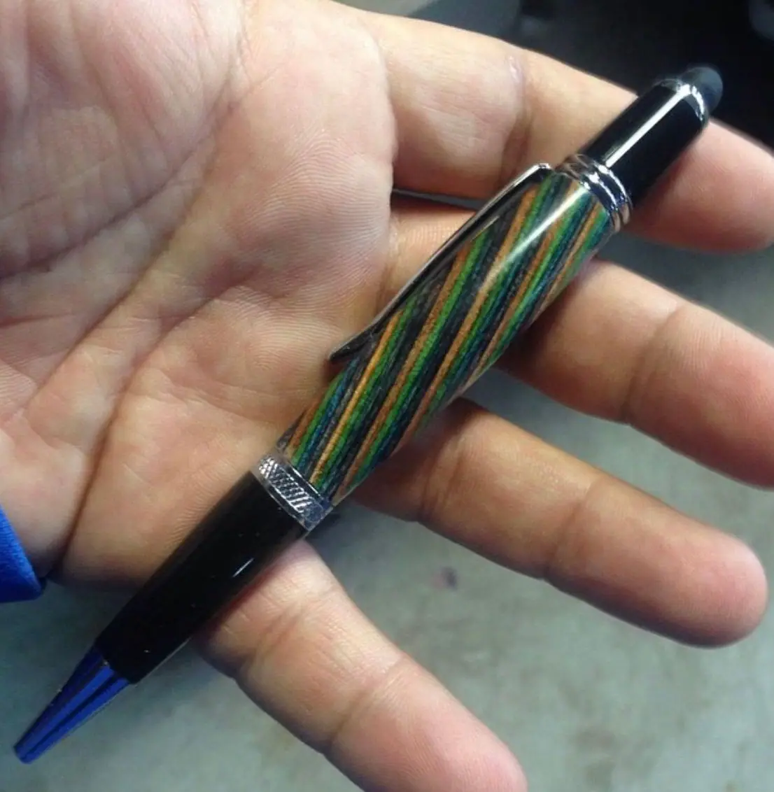 A pen with a barrel of green, orange and blue stripes, a black grip and chrome trim, held in an open palm.