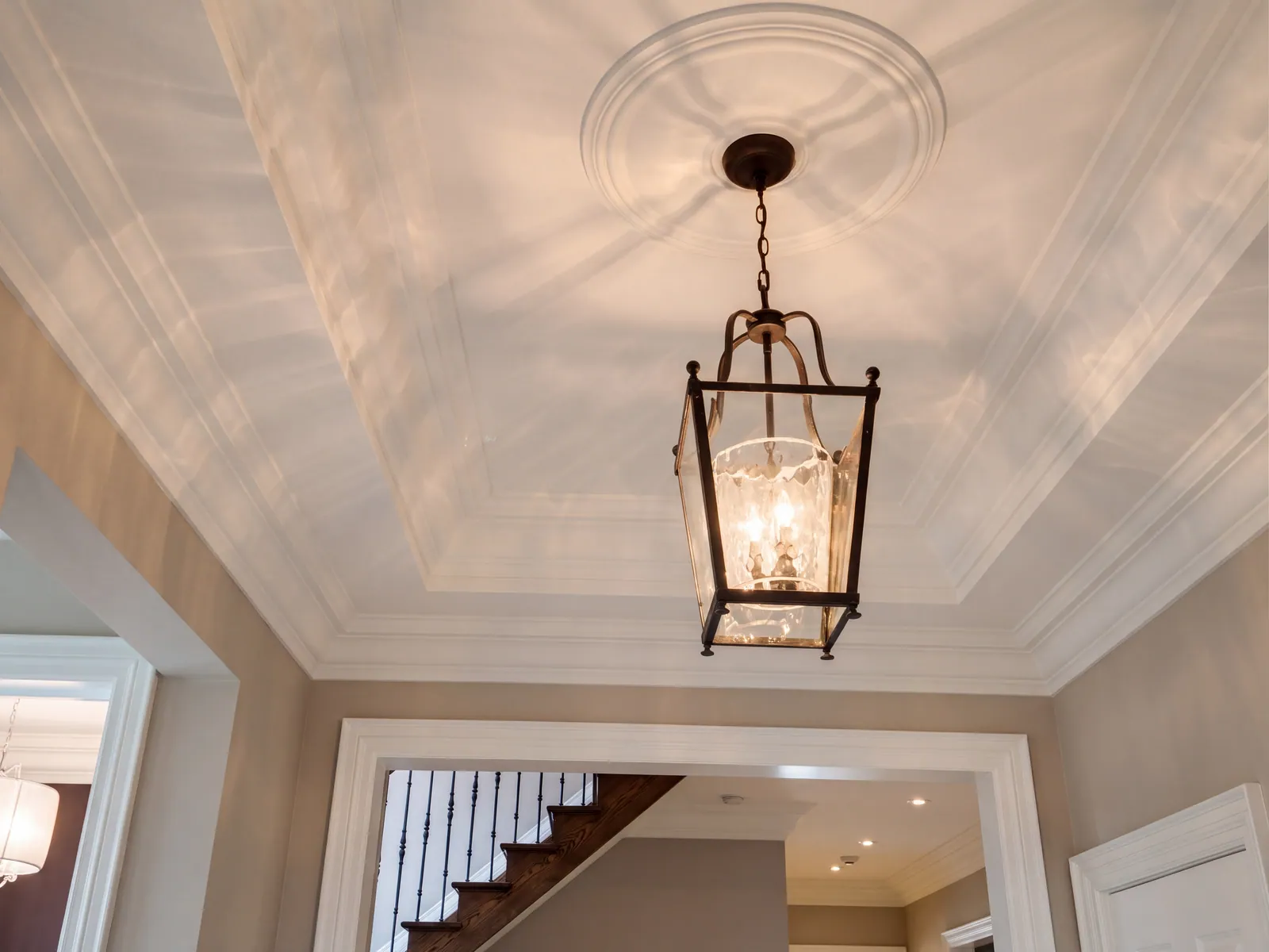 A tray ceiling with white trim and a round ceiling medallion, with a black lantern pendant light hanging below it.