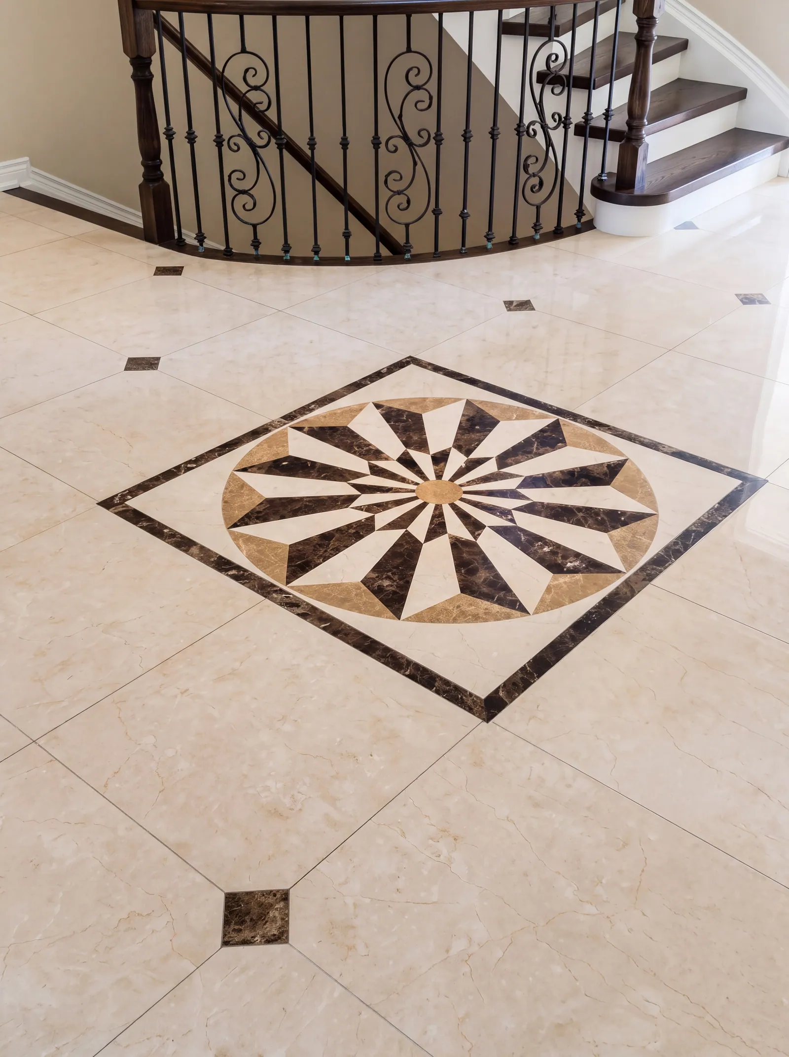 A polished cream stone floor with a star-shaped inlay of dark and pale stone in a square border, beside the foot of a stair with iron balusters.