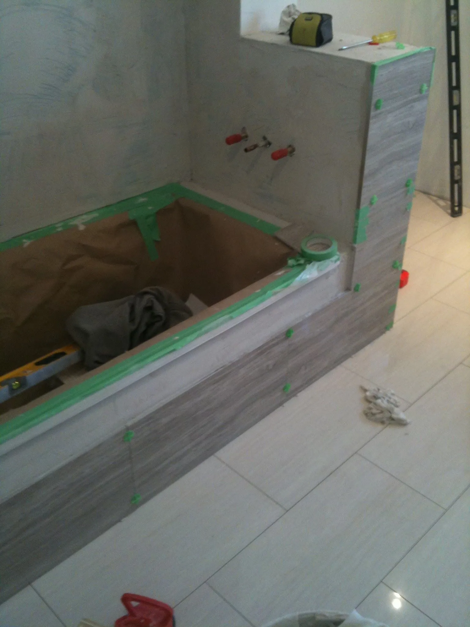 A tub surround being tiled, with green spacers along the edge.