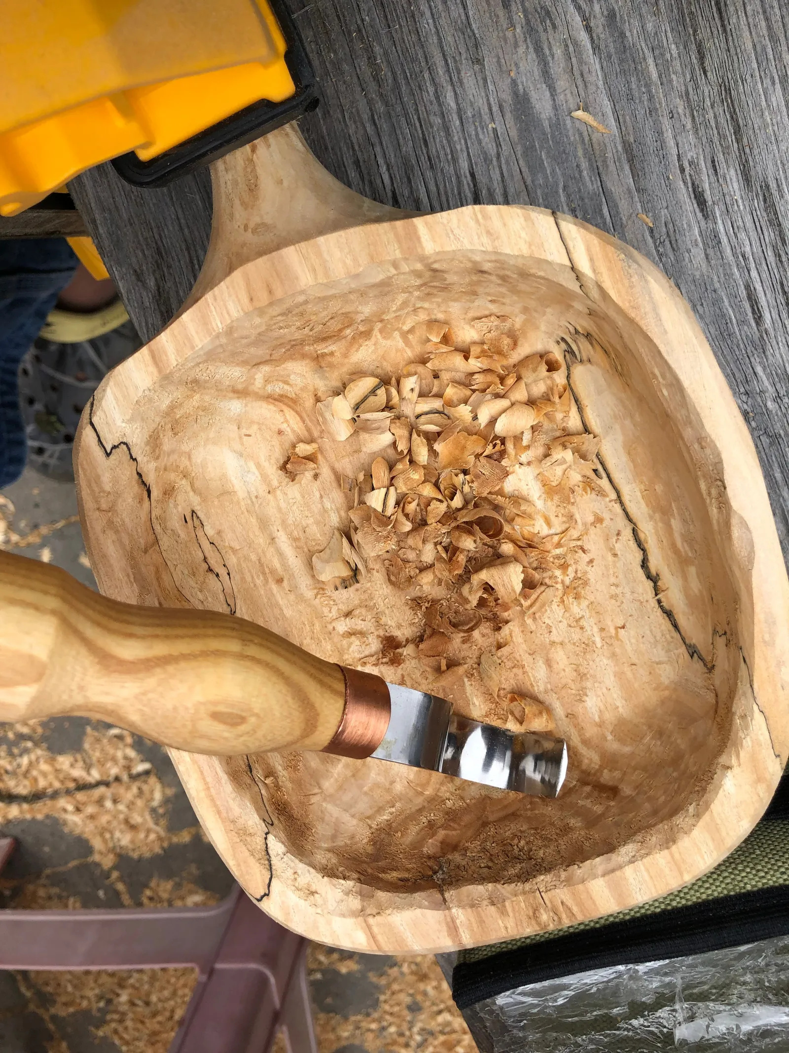 A bowl carved out of a wood blank, with shavings and tools.