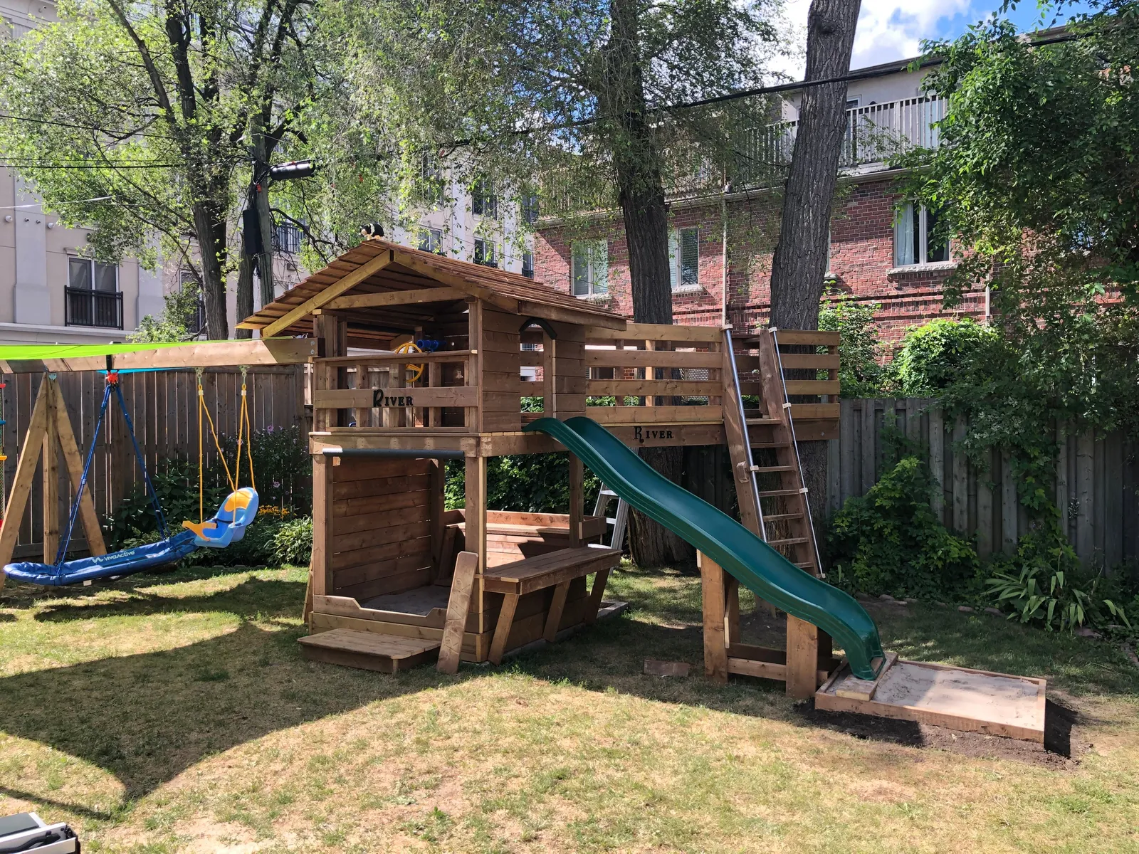 A wide view of the fort, the slide and the swing frame in the yard.