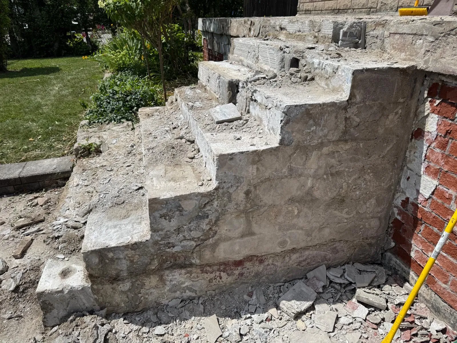 Old concrete steps broken down to their core beside a red brick wall, with rubble at the base.