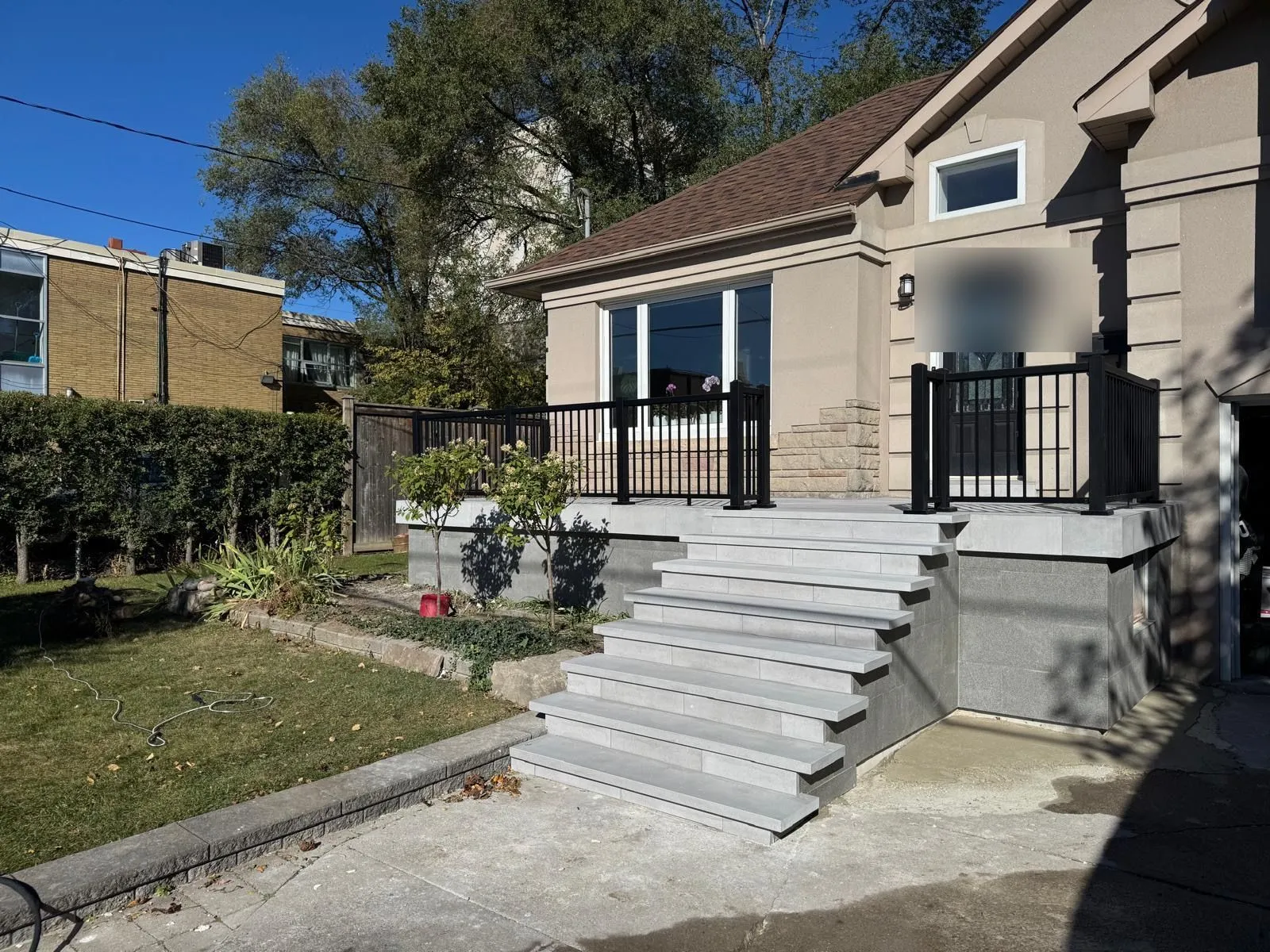 Pale grey steps rising to a landing with a black metal railing, in front of a stucco house.