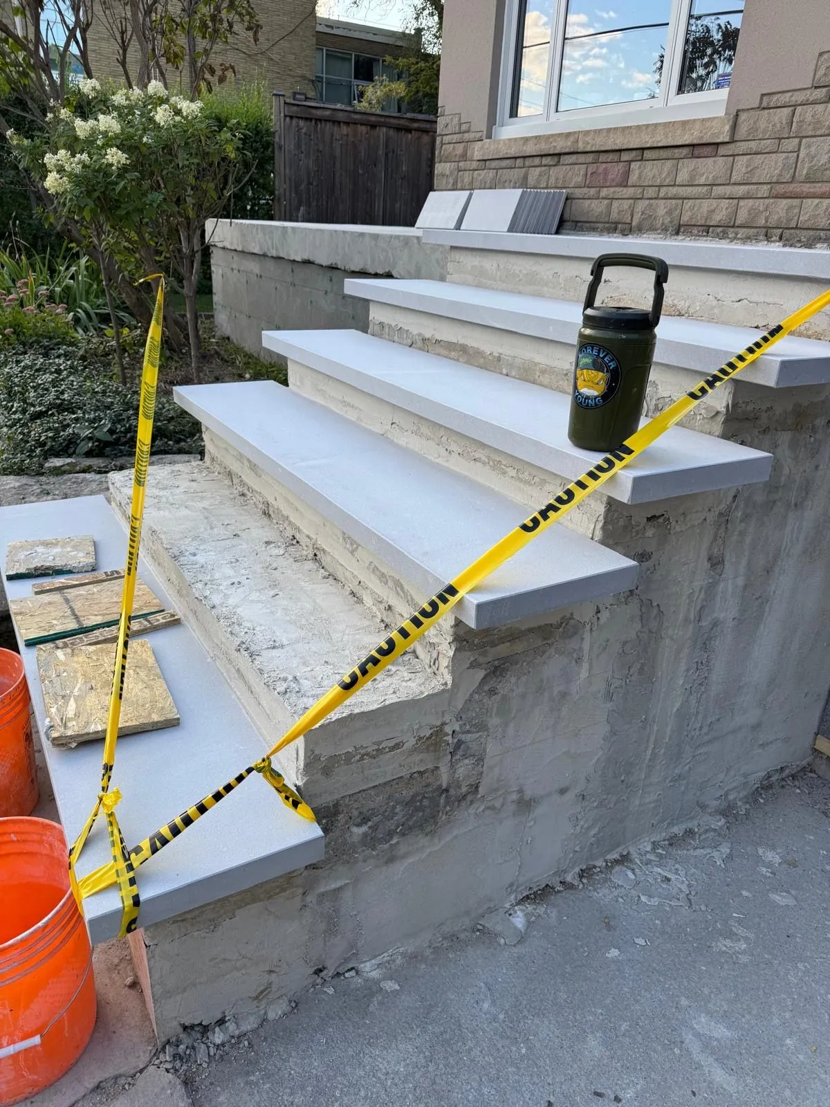 Pale stone treads set on concrete steps, with yellow caution tape and an orange bucket.