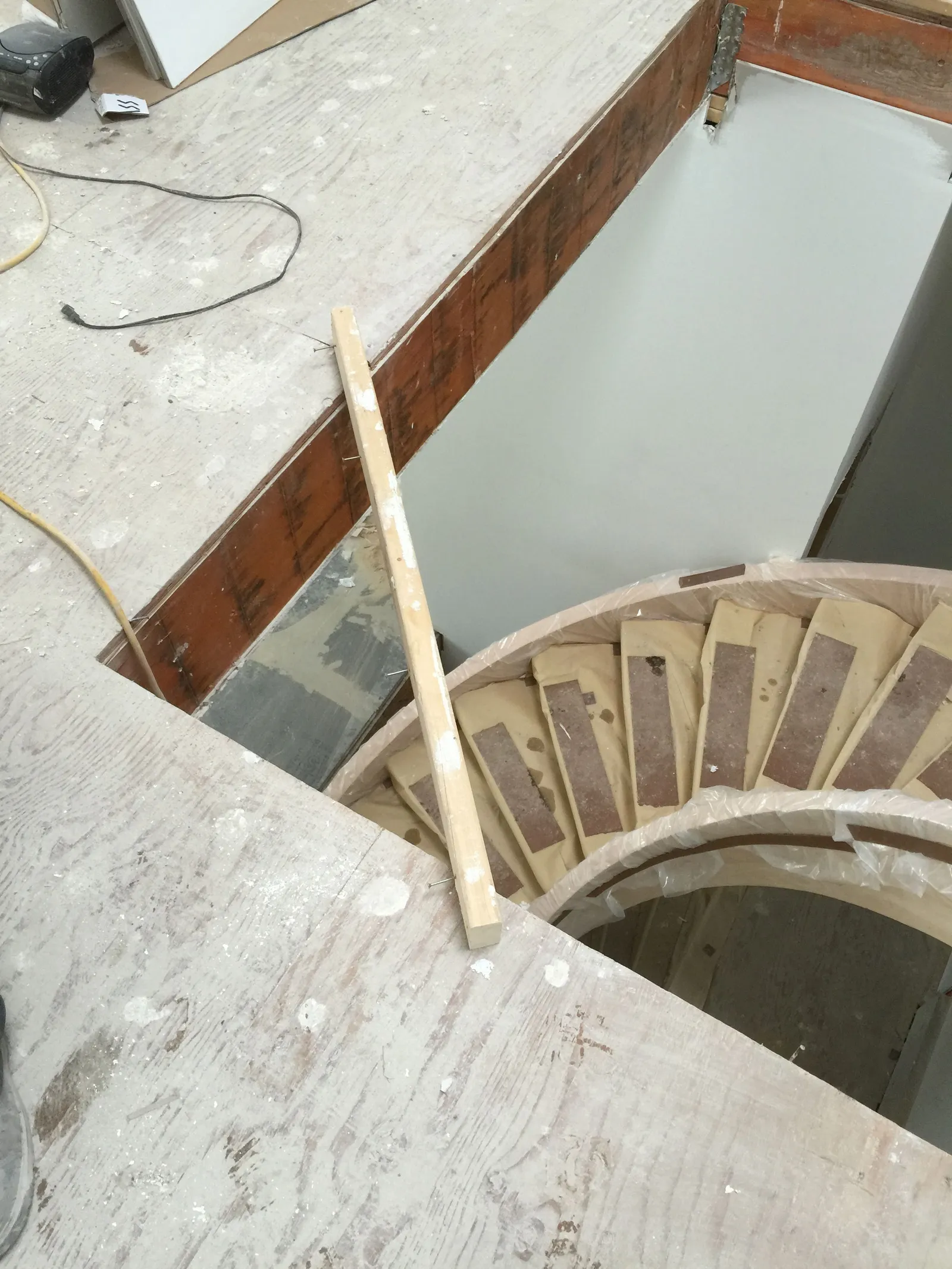 The framing of a curved stair seen from above, on a plywood floor.