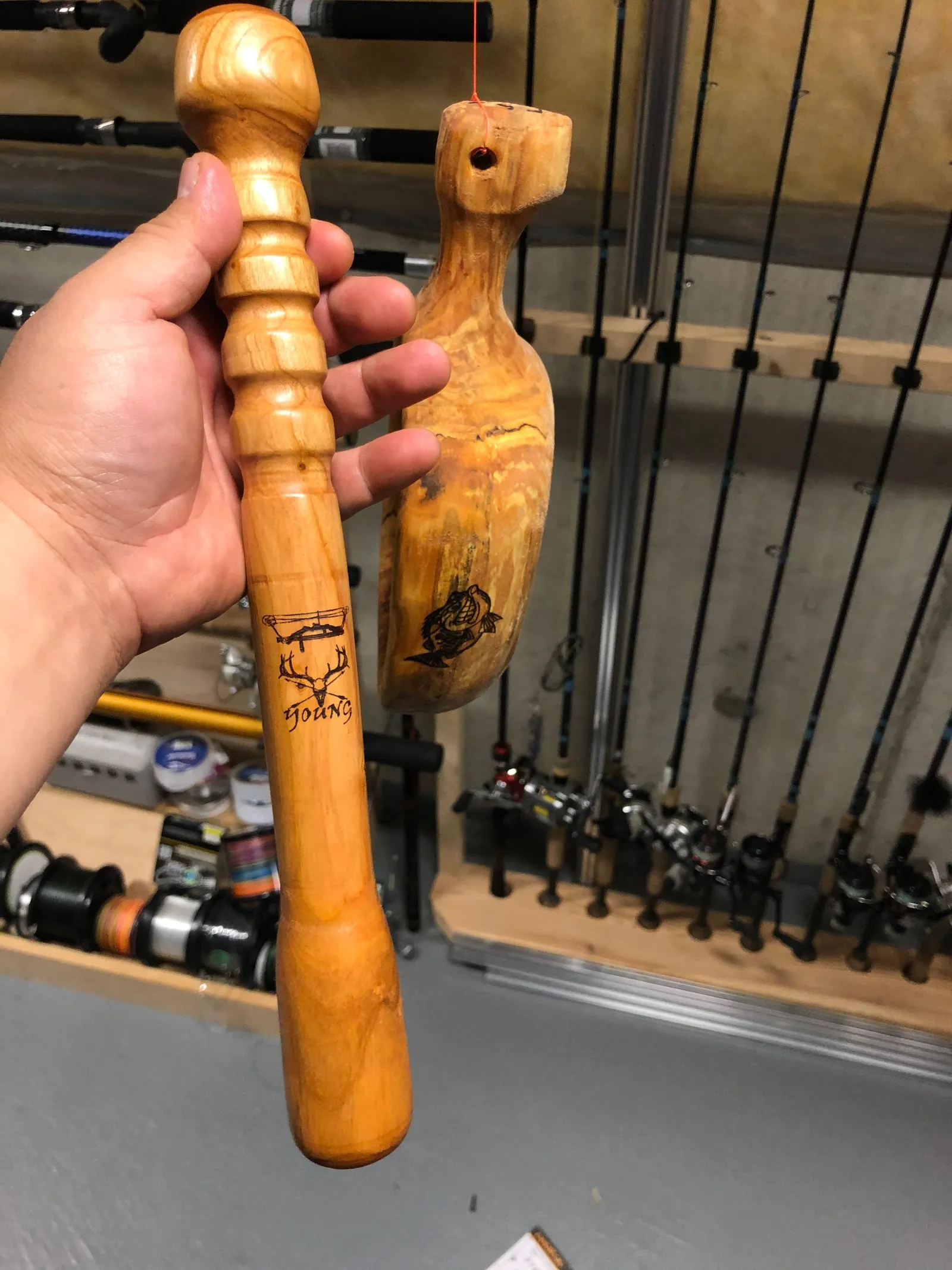 A turned wooden handle held in a hand, with a carved figure behind it.